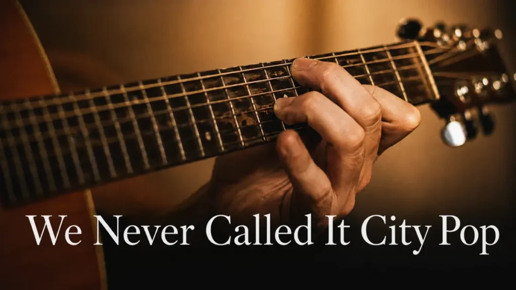 A hand on an acoustic guitar fretboard, fingers not yet settled into the chord — the physical difficulty of playing city pop harmony