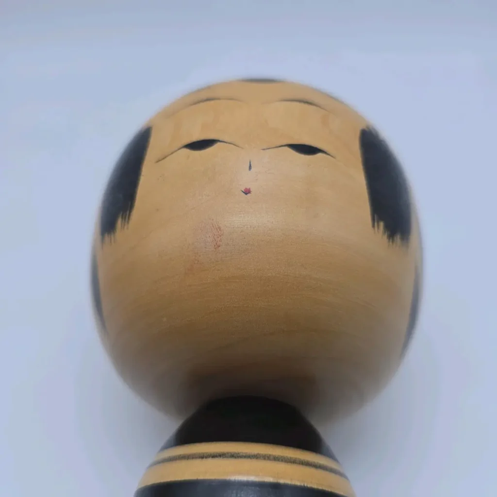 Close-up of a light-wood kokeshi doll's face, painted with a few quiet strokes