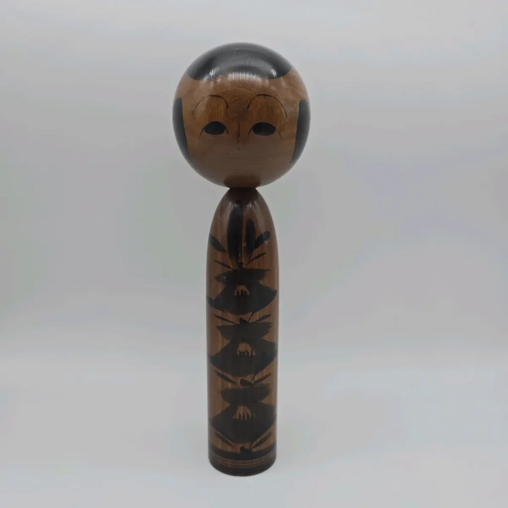 A dark-wood traditional kokeshi doll with black floral brushwork down its body